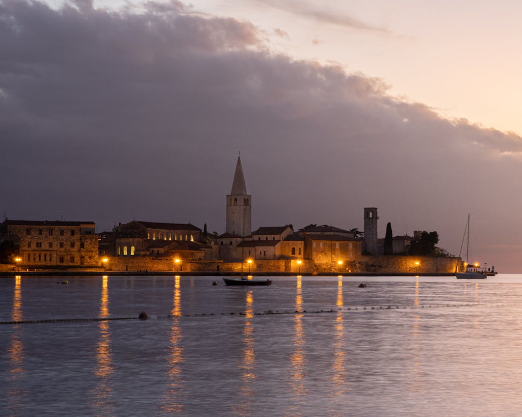 Peaceful evening scene of Poreč cityscape with illuminated waterfront and iconic towers.