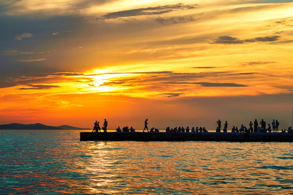 A vibrant sunset with silhouettes of people on a pier in Zadar, Croatia.