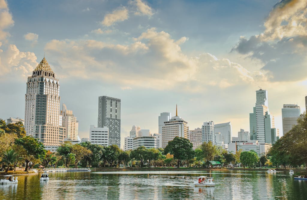 Scenic view of Bangkok's skyline with modern buildings, lake, and greenery under a blue sky.