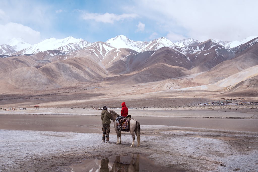 A serene moment captured at Pangong Lake, Ladakh, featuring horseback riding by snow-capped mountains.