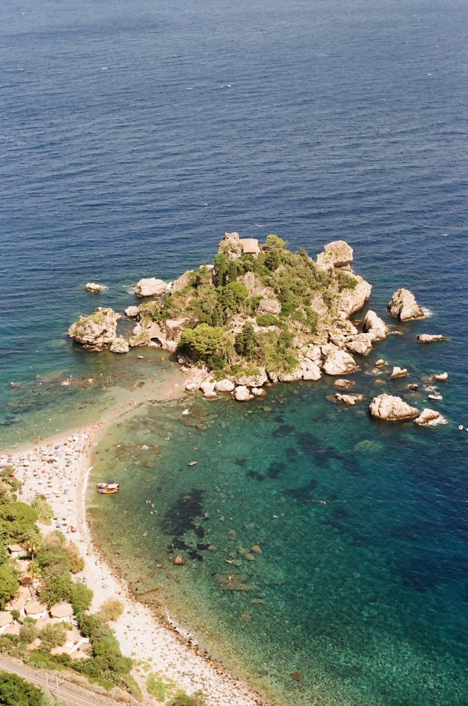 Explore the stunning aerial view of Isola Bella in Taormina, Sicily with vibrant blue waters and lush green island.